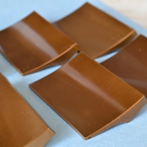 May include: Six brown, rectangular, curved cabinet knobs with a shiny finish.