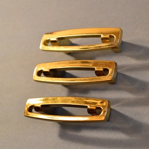 May include: Three gold-toned cabinet pulls with a rectangular shape and a long, narrow opening in the center.