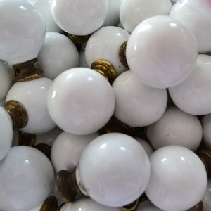 May include: A close-up of a group of white ceramic knobs with gold accents. The knobs are round and have a smooth finish.