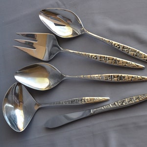 May include: A set of five silver serving utensils, including a slotted spoon, fork, spoon, ladle, and knife. The handles have a textured, geometric design. The utensils are arranged on a gray surface.