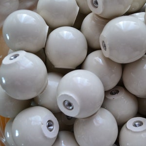 Peut inclure: Gros plan sur un tas de boutons en céramique blanc cassé. Les boutons sont ronds et ont une finition lisse et brillante. Chaque bouton a un petit trou au centre pour être fixé à un meuble.
