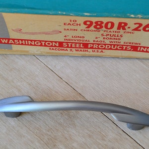 May include: A silver cabinet pull measuring 10 cm long with a 7.6 cm boring. The pull is labelled "980 R-26D" and is made of satin chrome plated zinc. The box also says "Washington Steel Products, Inc. Tacoma 2, Wash., U.S.A."