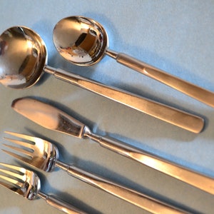 May include: A set of four silver utensils, including a spoon, a knife, and two forks, arranged on a light blue surface.