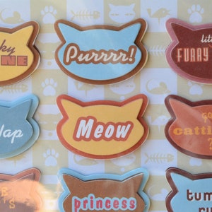 May include: Ten colorful cat-shaped stickers with different phrases, including "Frisky Feline", "Purrrr!", "Little Furry Friend", "Cat Nap", "Meow", "Got Cattitude", "The Cat's", "Princess", and "Tummy Rub".