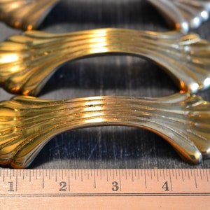 Peut inclure: Trois poignées de tiroir de cabinet dorées avec un design décoratif en forme d'éventail. Les poignées sont disposées en rangée, la poignée du haut étant légèrement floue.