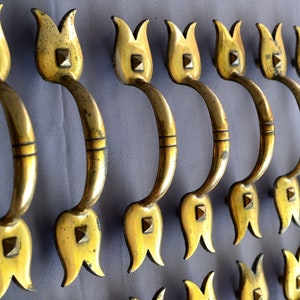 May include: A set of 10 antique brass cabinet door pulls with a tulip design. The pulls have a decorative nail head accent and a smooth, polished finish.