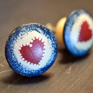 May include: Two wooden knobs with a blue and white painted design. Each knob features a red heart with a white scalloped edge.