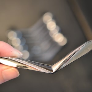 May include: A silver metal cabinet door handle with a curved, V-shaped design.