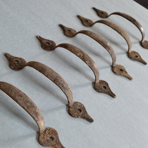 Peut inclure: Huit poignées de tiroir en métal de style antique avec un design pointu en forme de larme. Les poignées sont de couleur brun rouille et ont un aspect usé et vieilli.