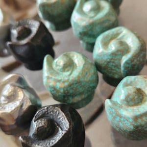 Peut inclure: Une collection de petits boutons décoratifs en céramique faits à la main dans différentes couleurs, notamment le noir, l'argent et le turquoise.