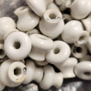 May include: A close-up of a pile of white ceramic knobs with a hole in the center. Some of the knobs have the word "Japan" printed on them.
