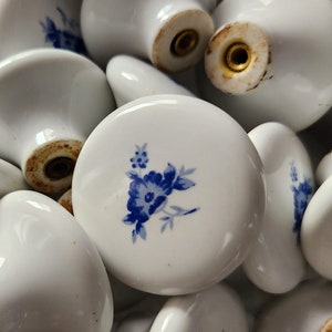Peut inclure: Un ensemble de boutons de cabinet en céramique blanche avec des motifs floraux bleus. Les boutons ont une base en métal doré.