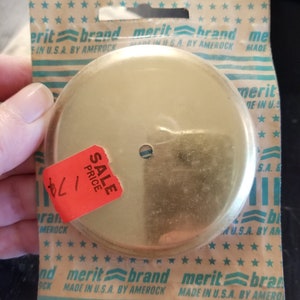 May include: A gold-colored metal round plate with a small hole in the center. The plate is packaged in a clear plastic bag with a white and blue striped background. The bag has the text "merit brand" printed on it. A red sticker with the text "SALE PRICE" is attached to the plate.