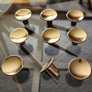 Peut inclure: Dix boutons de porte en or avec un dessus rond légèrement surélevé. Les boutons ont une finition lisse et brillante.