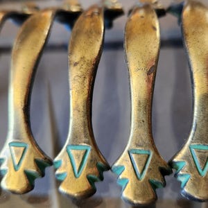 Peut inclure: Cinq poignées de porte d'armoire en laiton antique avec un motif géométrique vert turquoise. Les poignées sont en forme de poignée incurvée avec un motif triangulaire en bas.