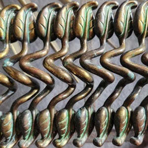 Peut inclure: Un ensemble de 10 tirettes de tiroir décoratives en laiton avec un motif de feuille. Les tirettes sont en forme de serpent ondulé et ont une finition patine verte.