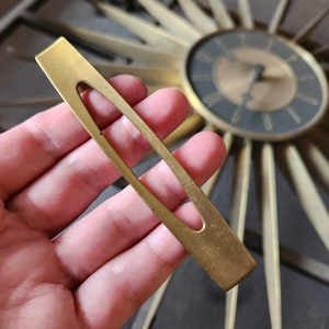 May include: A gold-toned metal drawer pull with a rectangular shape and a cut-out oval in the centre.