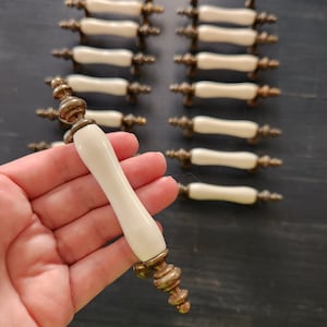Peut inclure: Un ensemble de 18 boutons de cabinet vintage avec un corps en céramique blanche et des accents en métal doré. Les boutons ont un design simple et élégant et seraient un excellent ajout à toute cuisine ou salle de bain.