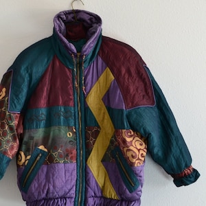 May include: A multi-colored puffer jacket with a geometric patchwork design. The jacket features a zipper closure, a high collar, and a drawstring waist.