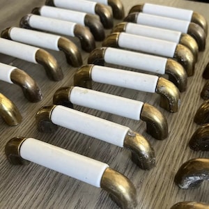 May include: A collection of white ceramic cabinet knobs with gold metal bases. The knobs have a rounded, slightly curved shape.