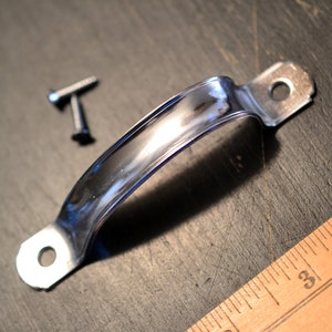 May include: A chrome-plated metal handle with two screw holes. The handle is curved and has a smooth, polished finish.
