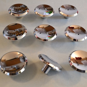 May include: Eight shiny chrome cabinet knobs with a rounded, slightly raised edge. The knobs are arranged in a grid pattern on a white surface.
