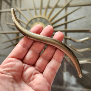 May include: A gold-toned metal cabinet hardware pull with a curved, S-shaped design.