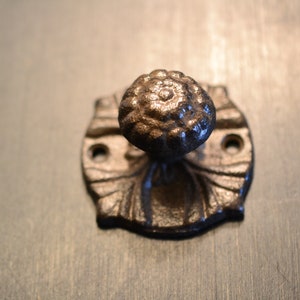 May include: A black cast iron door knob with a decorative floral design. The knob is mounted on a round plate with a scalloped edge.