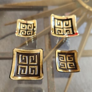 May include: Four gold-colored metal drawer pulls with a black geometric design. The pulls are in different sizes and shapes.