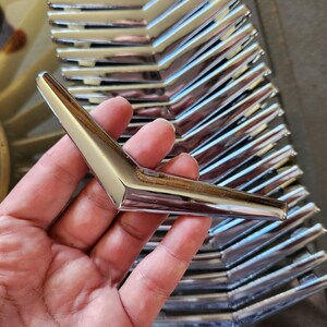 May include: A close-up of a stack of shiny, silver, V-shaped metal hooks. The hooks are arranged in a neat row, with the points of the Vs facing the same direction.