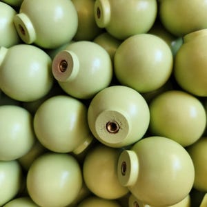 Peut inclure: Gros plan de plusieurs boutons de porte ronds en bois vert clair. Chaque bouton a une base plate et circulaire et un insert à vis de couleur laiton. Les boutons sont espacés uniformément et semblent neufs. Les boutons sont vert pâle.