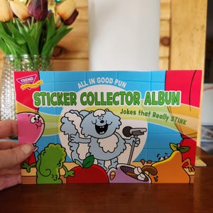 May include: A colorful sticker collector album with the text "ALL IN GOOD PUN" and "STICKER COLLECTOR ALBUM Jokes that Really STINK." The cover features cartoon characters and a light blue background.