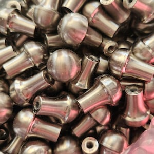 May include: A close-up shot of a pile of small, silver-colored metal knobs. Each knob has a rounded top and a cylindrical base. The knobs are densely packed together, filling the frame. The metal has a slightly reflective surface.