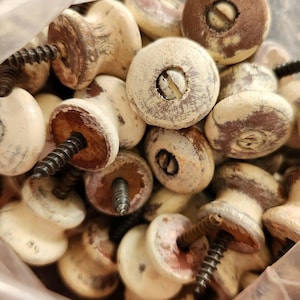 May include: A close-up of a pile of wooden knobs with a distressed white paint finish. The knobs have a screw hole in the center and are perfect for adding a vintage touch to furniture.