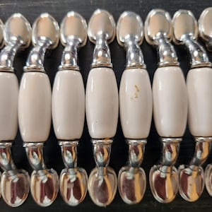 May include: A collection of vintage spoons with white ceramic handles and silver-toned metal spoon heads. The spoons are arranged in a row, showcasing their elegant design and classic aesthetic. The handles have a smooth, oval shape.