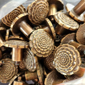 May include: A collection of antique bronze cabinet knobs. Each knob features a detailed floral design on the face and a cylindrical stem. The knobs have a warm, aged patina, suggesting they are vintage or vintage-inspired.