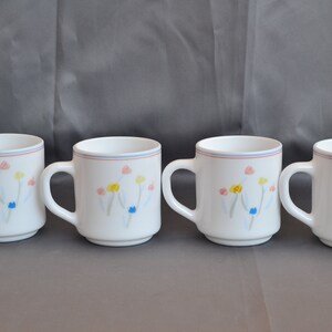 May include: Set of four white ceramic mugs with a floral design. The flowers are painted in shades of pink, yellow, blue, and green.