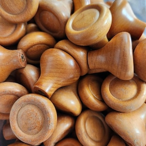 May include: A close-up shot of a pile of wooden knobs. The knobs are a warm, medium brown color and have a variety of shapes, including rounded and mushroom-shaped designs. The wood grain is visible, adding texture to the image.