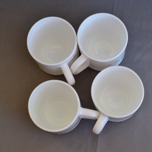 May include: Four white ceramic coffee mugs with a floral design. The mugs are empty and have a light brown background with a yellow and blue floral pattern.