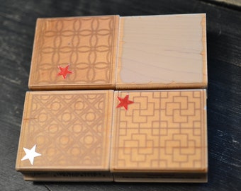 May include: Four wooden stamps with different geometric patterns. The stamps are arranged in a grid pattern. The top left stamp has a red star on it. The top right stamp is blank. The bottom left stamp has a white star on it. The bottom right stamp has a red star on it.