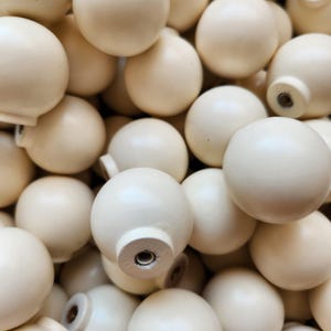 Peut inclure: Gros plan sur un tas de boutons de meubles sphériques de couleur crème. Chaque bouton a une forme arrondie avec une base plate et un insert fileté pour la fixation. Les boutons sont étroitement tassés, remplissant le cadre.