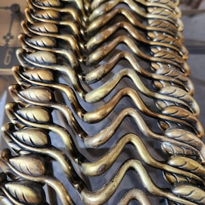May include: A close-up of a set of decorative metal drawer pulls. The pulls are made of brass and have a wavy, leaf-like design.