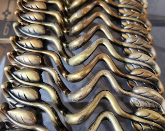 May include: A close-up of a set of decorative metal drawer pulls. The pulls are made of brass and have a wavy, leaf-like design.