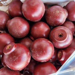 May include: A close-up of several dark red wooden knobs. Each knob is round with a flat base and a central hole. The knobs have a slightly aged look, with a deep burgundy colour. They are likely for furniture or cabinet doors.
