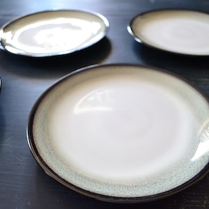 May include: A set of five ceramic dinner plates with a brown and green glaze. The plates have a white center and a dark brown rim.