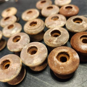 May include: A collection of 15 wooden spools with a hole in the centre. The spools are various shades of brown and have a worn, rustic look.