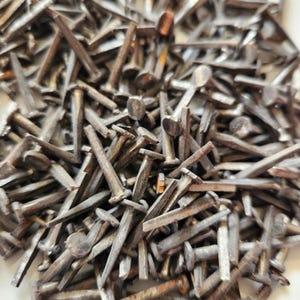 May include: A large pile of antique metal tacks or nails. The tacks are all silver in color and have a variety of sizes and shapes.