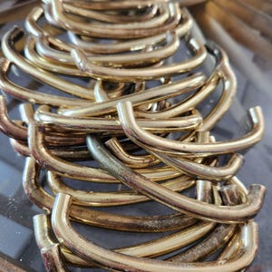 May include: A close-up of a collection of gold-coloured metal handles. The handles are curved with a rounded shape and a hook-like design. The metal has a shiny, reflective surface.