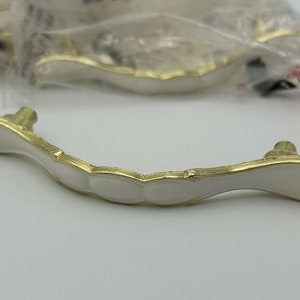 May include: White cabinet knob with a gold trim and a scalloped design.