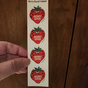 May include: A strip of four stickers featuring a smiling red strawberry with green leaves. Each sticker has the words "BERRY GOOD" and a star logo. The text "Berry Good T-83601" is printed at the top.